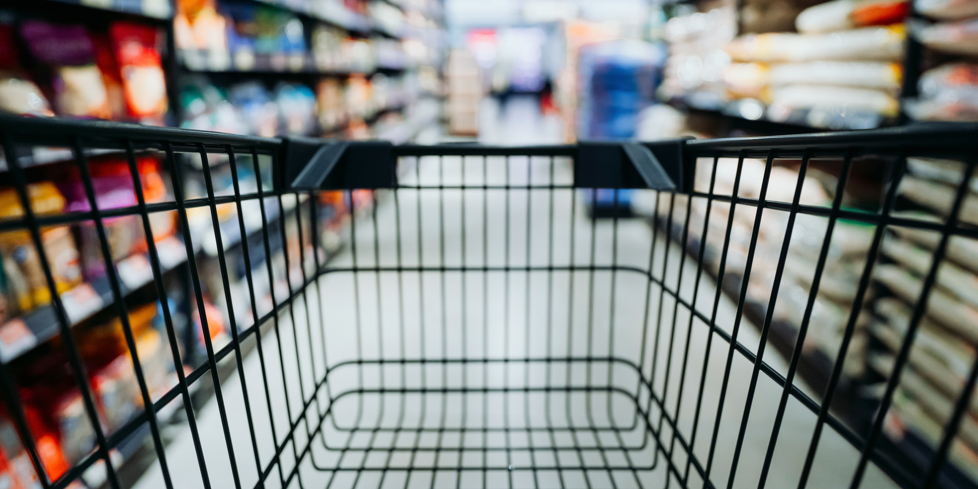 Personal perspective of a shopper pushing shopping trolley along product aisle while shopping in a supermarket