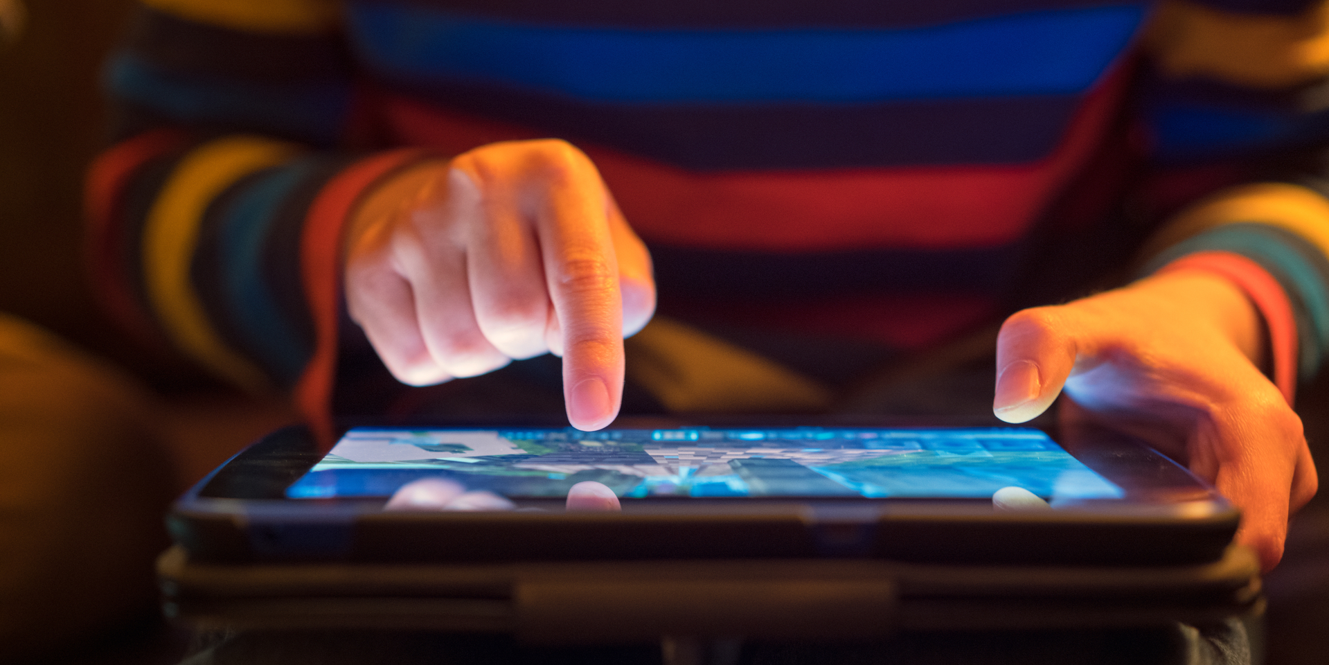 Close up of a young boy using a tablet computer, his finger hovering over it as he's about to touch the screen.