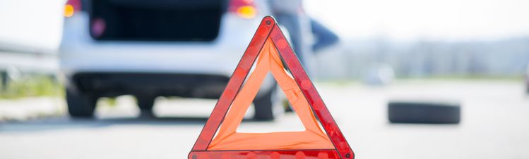 Medium angle of roadside safety triangle in foreground with person standing next to car in background.