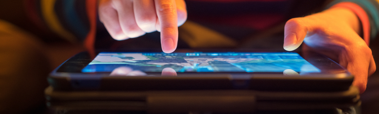 Close up of a young boy using a tablet computer, his finger hovering over it as he's about to touch the screen.