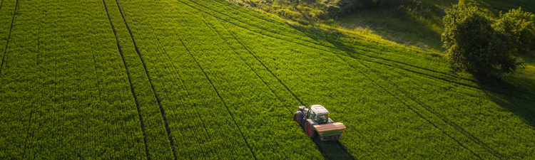 Aerial view on agricultural landscape in spring. A farmer with his machine is driving on a wheat field. Captured with a drone in southern Germany.