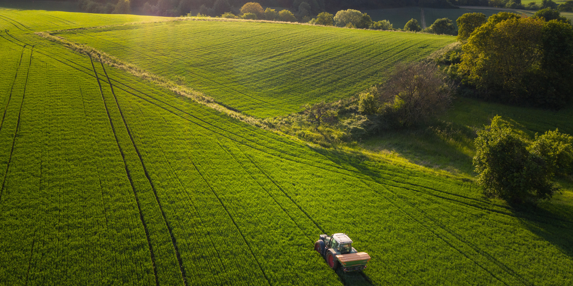 Aerial view on agricultural landscape in spring. A farmer with his machine is driving on a wheat field. Captured with a drone in southern Germany.