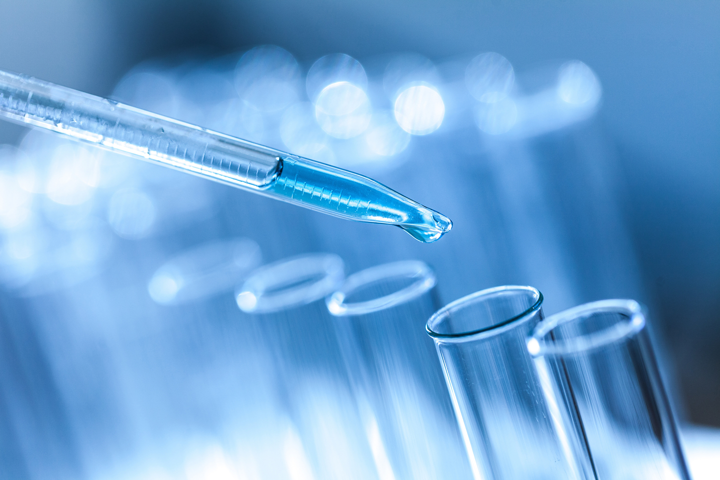 Close-up of blue liquid in pipette dripping into test tube.