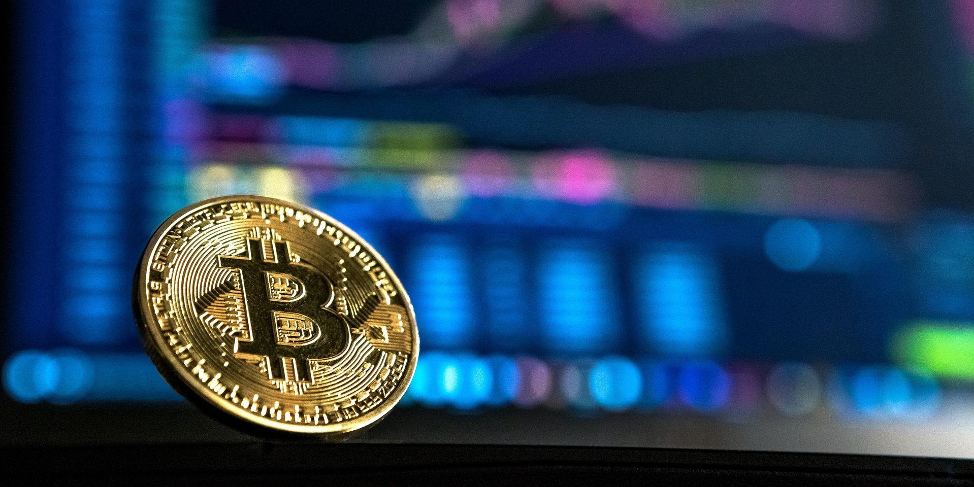 Close-up of gold bitcoin with computer screen blurred in the background.