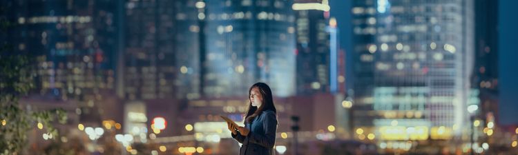 Young businesswoman using digital tablet in financial district, against illuminated corporate skyscrapers at night