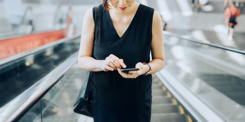 Medium angle of young woman looking at smartphone while riding an escalator.