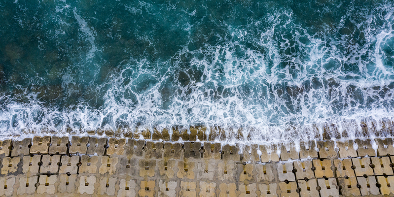 Aerial of waves hitting an anti-flood seawall constructed of concrete cubes.