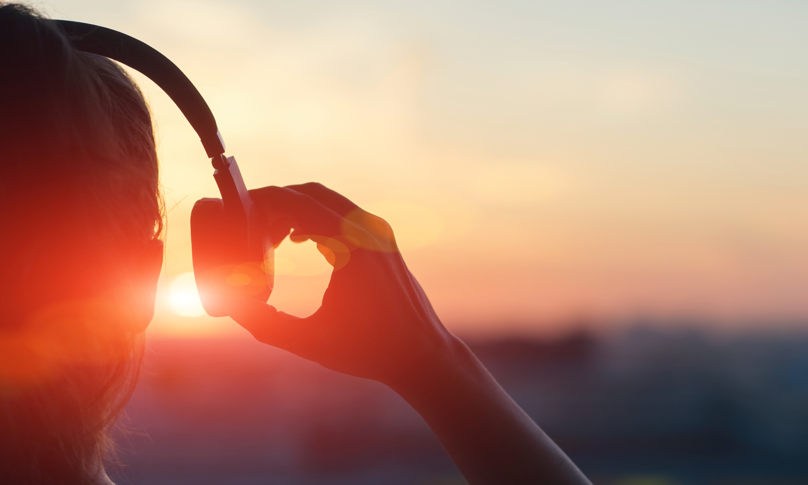 Close-up of woman wearing headphones with sun in background.