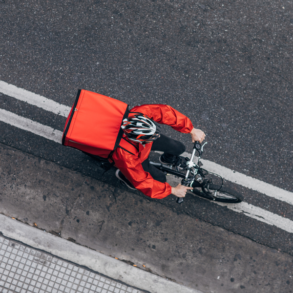 Bike delivery rider on bike carrying red cooler on his back.
