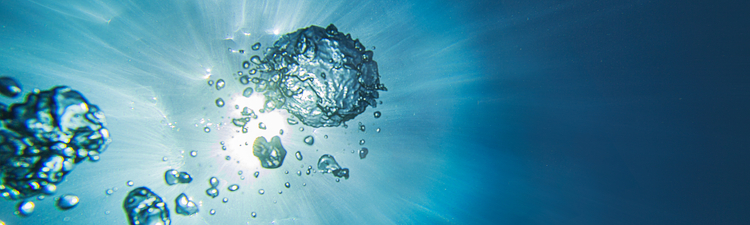 Close-up of sunlight filtering through water with bubbles ascending.