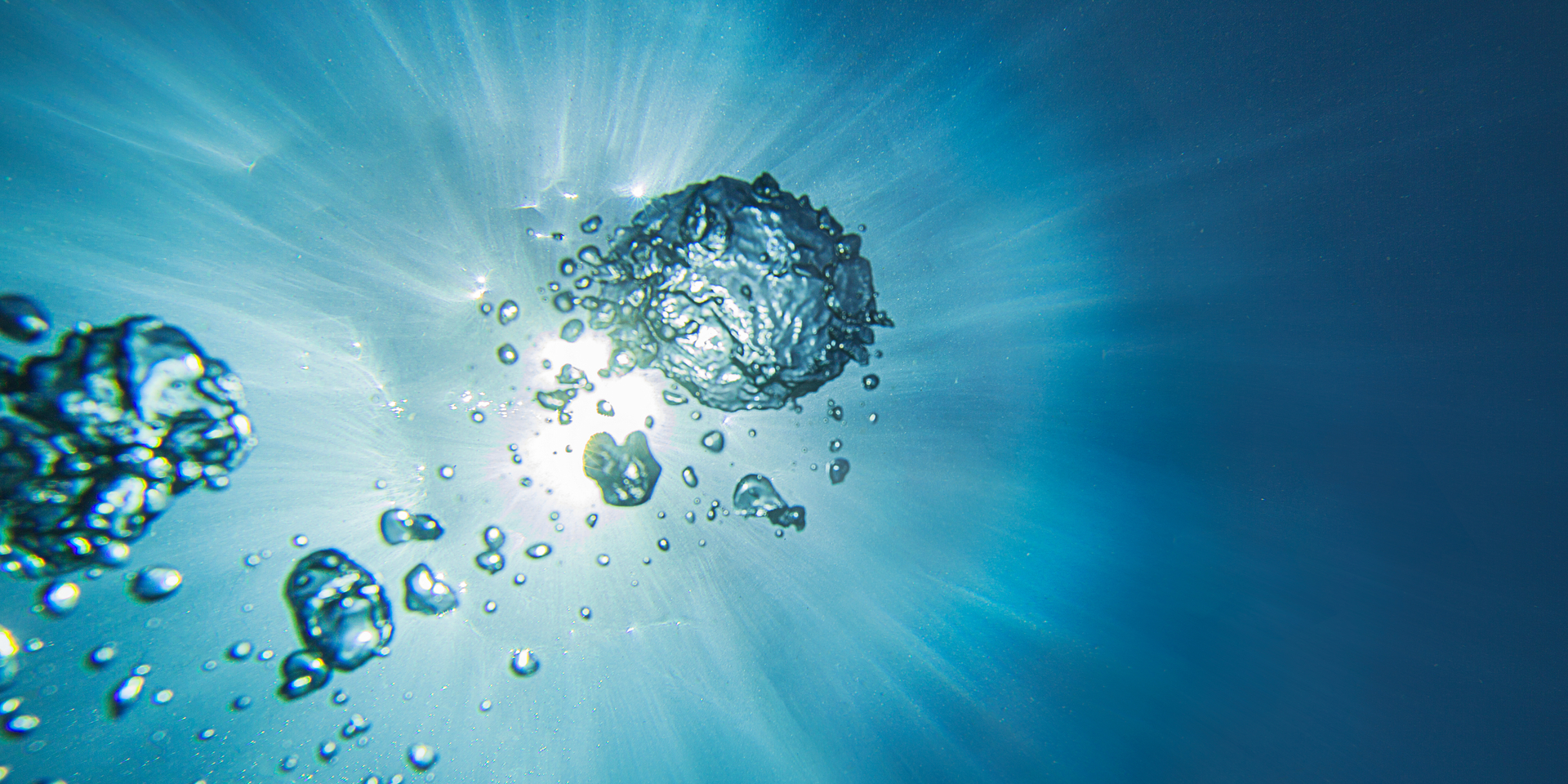 Close-up of sunlight filtering through water with bubbles ascending.