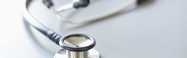 Close-up of stethoscope on desk with doctor's hands using laptop. The female doctor is sitting at desk in office. The focus is on stethoscope.