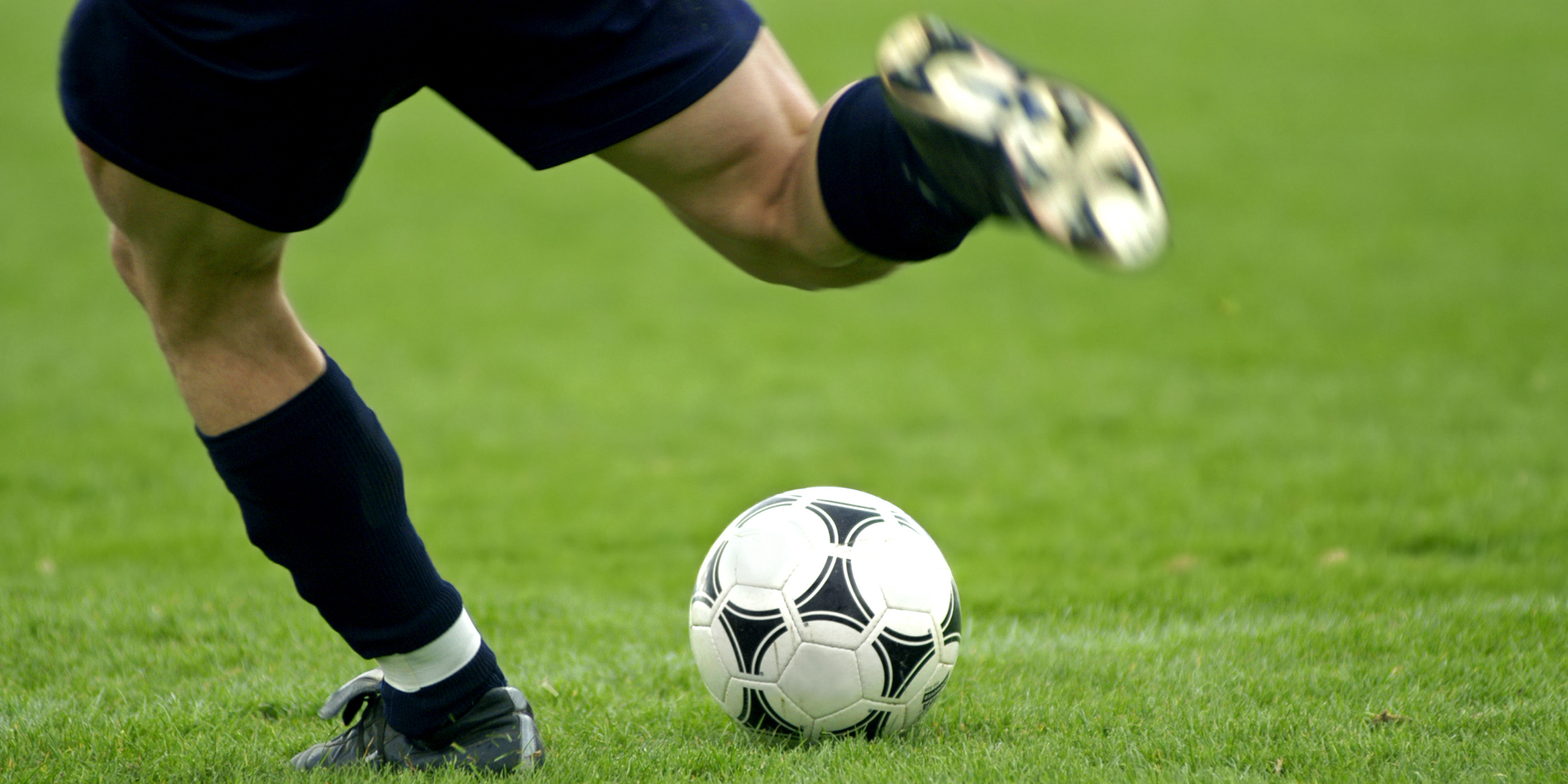 Close-up of soccer player kicking soccer ball.