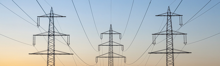 Wide angle of high voltage power lines over a field at sunset.