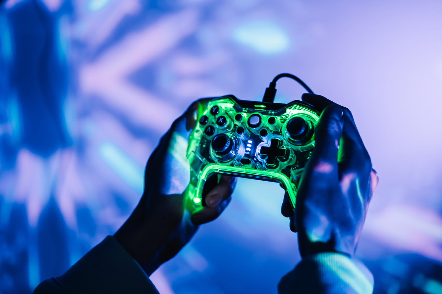 A man with a neon joystick in the dark playing video game on a computer.