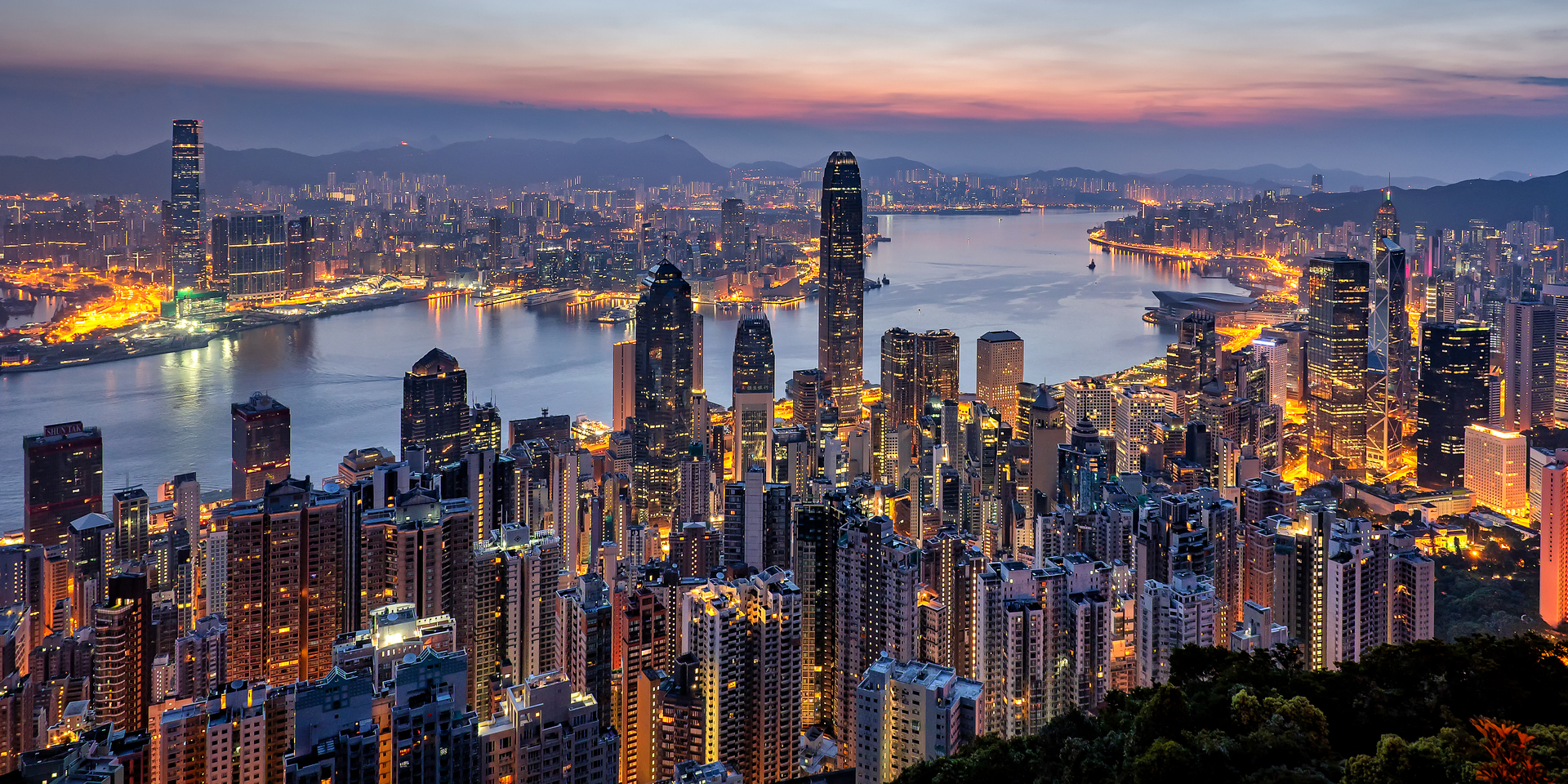 Wide angle of Hong Kong city skyline and Victoria Harbor at dusk.