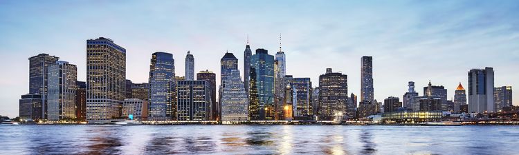 Panoramic view of Manhattan skyline at dusk from East River and Brooklyn Bridge Park.