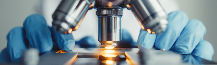 Close-up of scientist examining slide under a microscope.