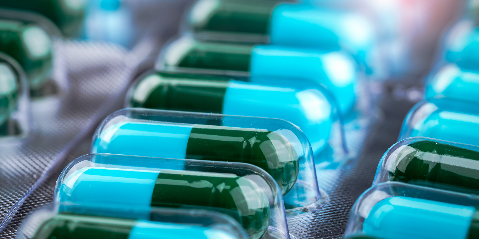 Close-up of green and blue pill capsules in blister pack.