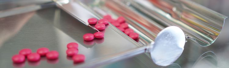 Close-up of pink tablet pills on metal pill counting tray.