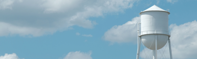 Wide angle of white water tower against blue sky and clouds.