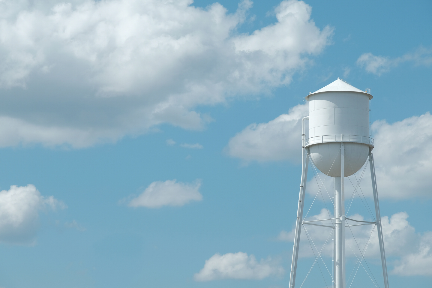 Wide angle of white water tower against blue sky and clouds.