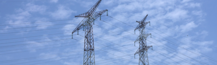 Medium angle of high-voltage transmissions tower against blue sky.