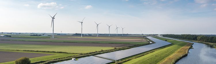 Aerial of solar panels and wind turbines positioned near river or creek.