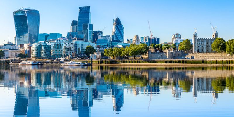 Wide angle of London's financial district skyline with Thames River in foreground.