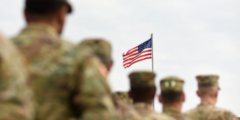 Medium angle of uniformed soldiers standing in front of American flag.