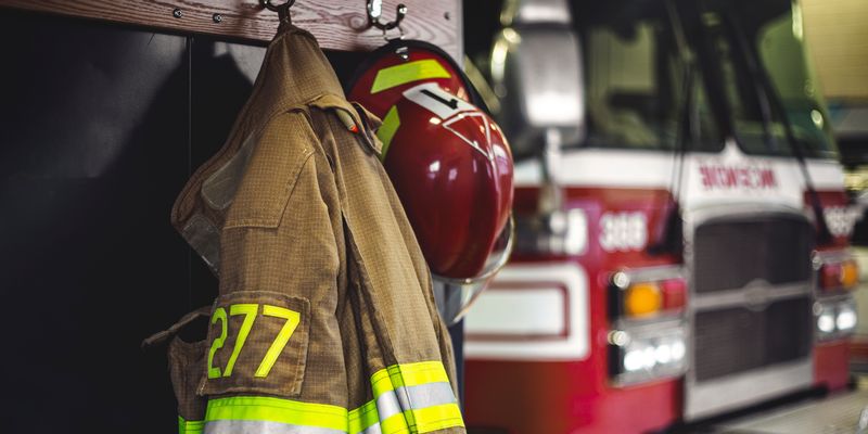 Medium angle of firefighter's uniform hanging in fires station with fire truck in background.