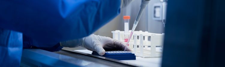 Close-up of technician working with pipette and multi-well plates in laboratory.