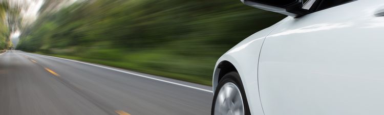 Medium angle blurred motion of sedan car driving on rural road.