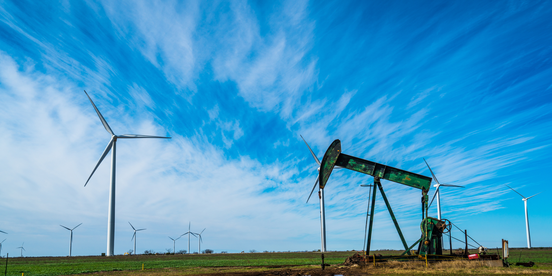 Oil platform pumping oil out of the ground near Lubbock , Texas in West Texas with wind turbines all around in a huge wind farm one of the worlds largest wind farms in sweet water , Texas