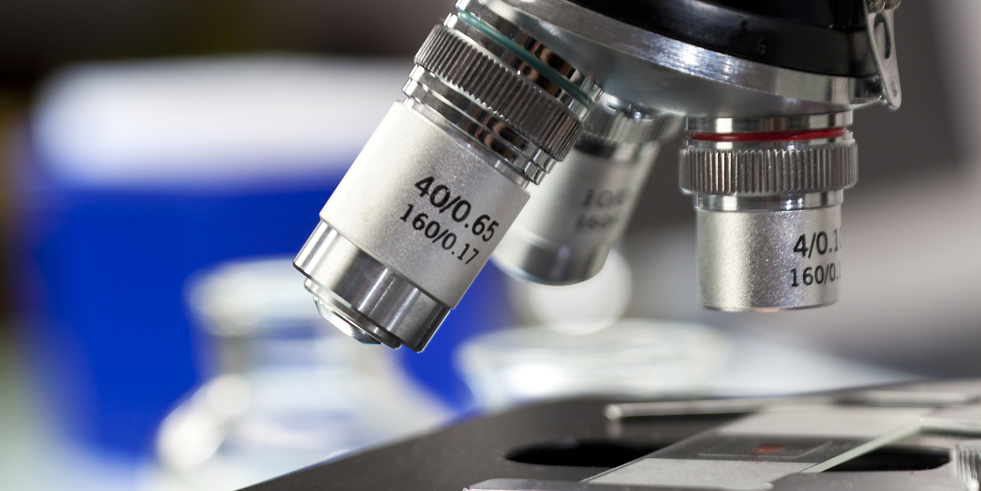 Close-up of microscope in laboratory with flasks visible.