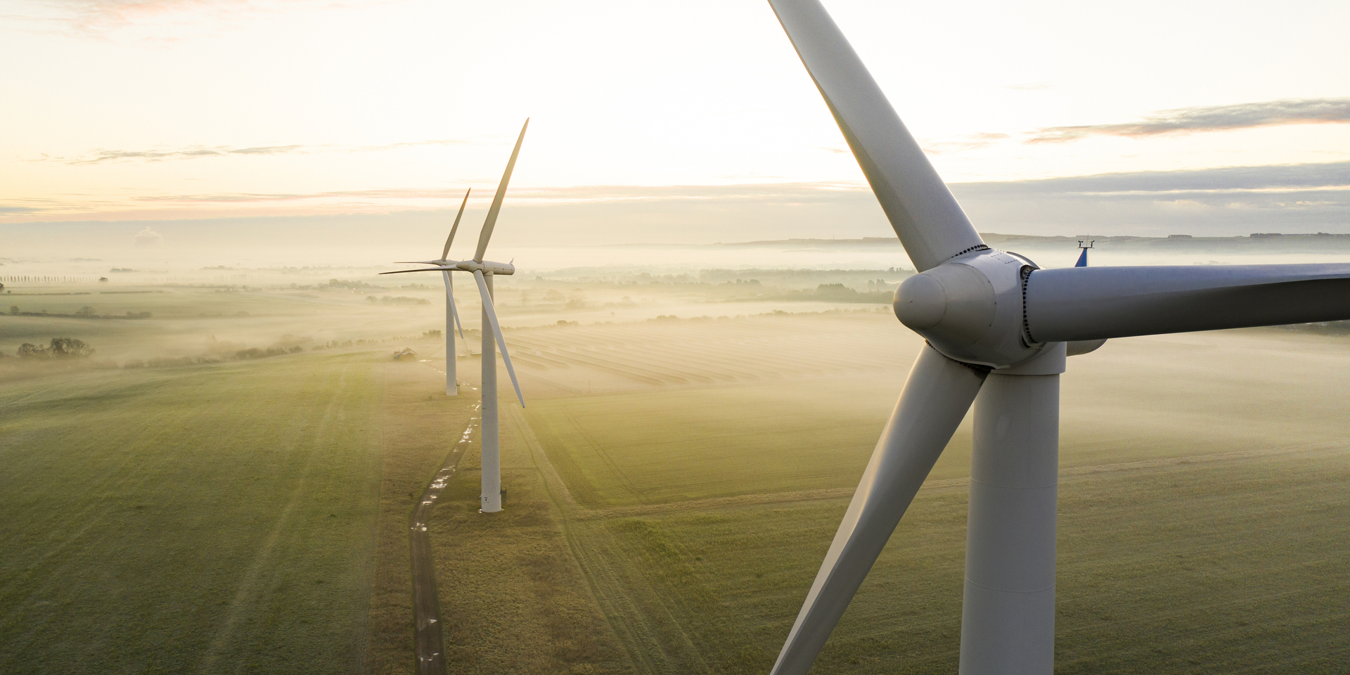 Aerial view of three wind turbines in the early morning fog at sunrise in the English countryside