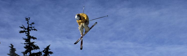Wide angle of skier jumping mid-air near snow embankment.