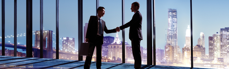 Multi-Ethnic Businessmen Shaking Hands Indoors With City As A Background