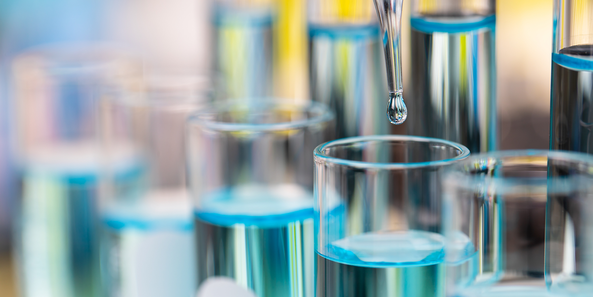 Drop of clear blue liquid from droper droping to test tube in laboratory with bright color blur background.