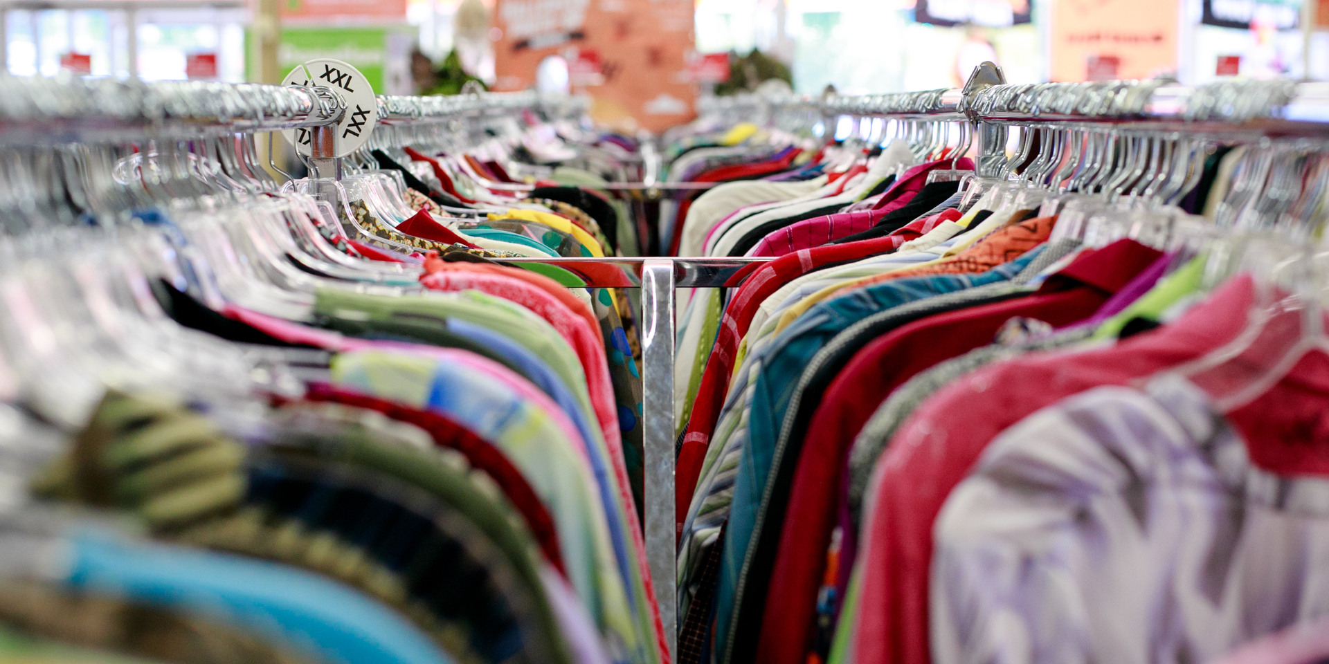 a variety of colorful shirts hang on a clothing rack at a thrift store
