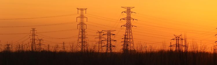Medium angle of silhouetted high-voltage transmissions towers against orange sky.