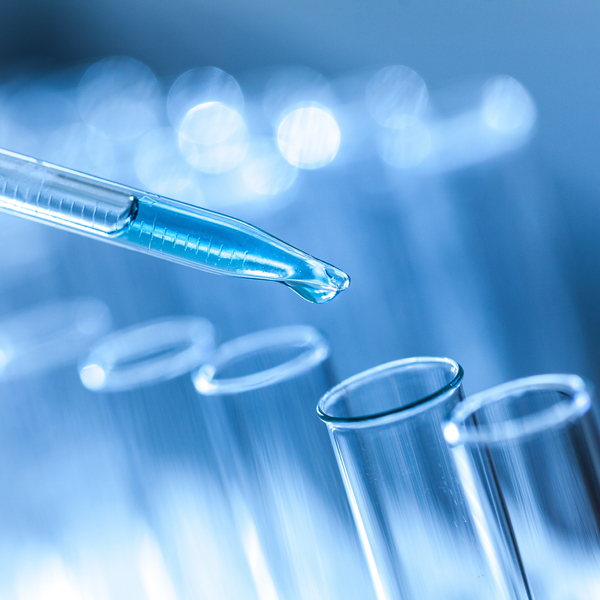 Close-up of blue liquid in pipette dripping into test tube.