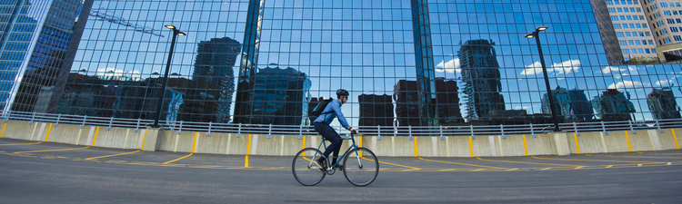 Wide angle of person on bicycle riding in parking lot next to office building.