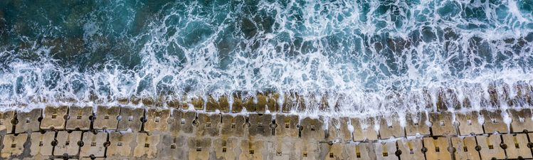 Aerial of waves hitting an anti-flood seawall constructed of concrete cubes.