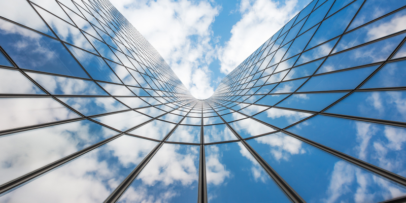 Up angle of blue sky and clouds reflected on curved glass building.