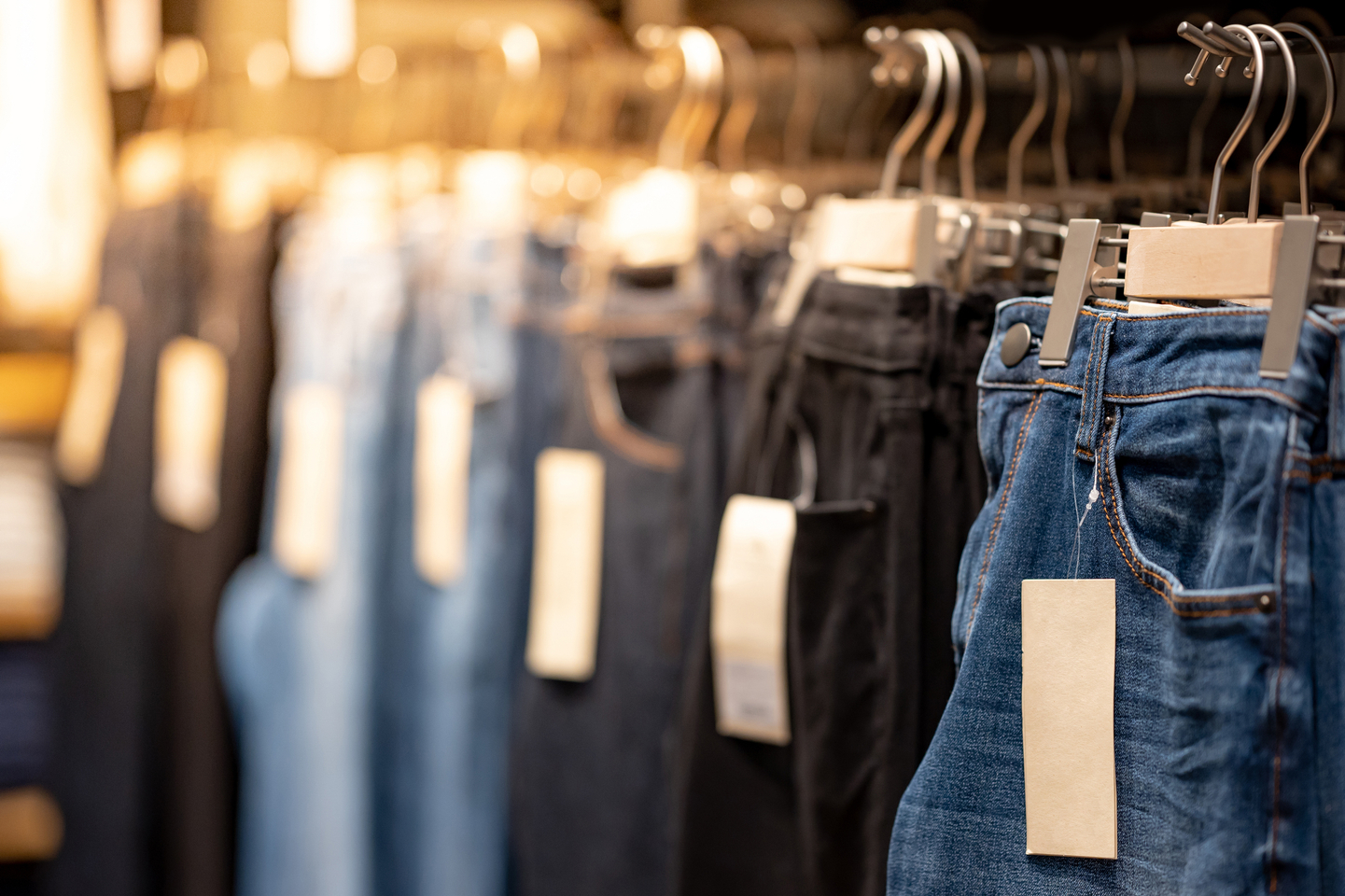 Close-up of denim jeans in varying colors hanging on clothes rack.