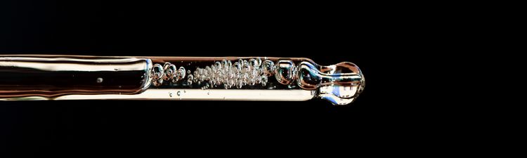 Close-up of glass pipette filled with transparent liquid.