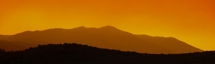 Wide angle of mountain range silhouetted against orange sky.