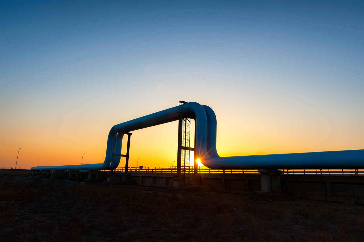 Wide angle of steel pipelines outside an oil refinery at sunset.