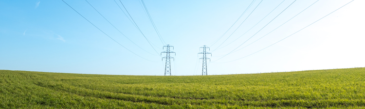 Large pylons with power lines stretching across a green grass field against a blue sky